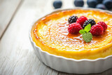 Delicious creme brulee decorated with berries and mint in white ceramic dish