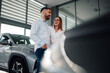 © Zamrznuti tonovi - Pair reviewing car beside sleek car in glossy dealership room