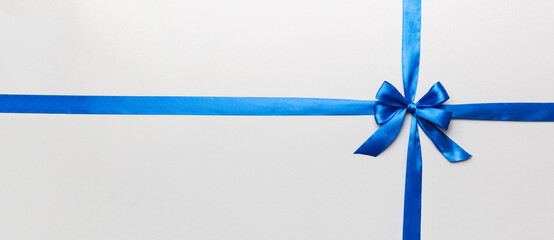 Wall Mural - Top view of blue ribbon rolled and blue bow isolated on colored background. Flat lay with copy space