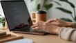 © ไมโต คอนเดรีย - Close-up of hands typing on a laptop keyboard, surrounded by productivity tools like a branded coffee mug,