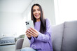 © deagreez - Young woman in stylish pullover smiling with excitement at phone indoors