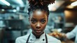 © Seyyar - Young black female chef in professional attire showcasing confidence and focus in a bustling kitchen environment, embodying culinary dedication and skill.