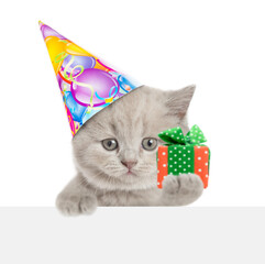 Poster - Cute tiny kitten wearing party cap holding gift box above blank white banner. isolated on white background.