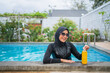© Odua Images - An elegant woman in modest swimwear relaxes by the poolside with a refreshing drink