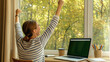 © Katewaree - Young woman celebrating a successful workday at home, expressing joy and relief while sitting at her desk with a view of a serene autumn landscape through the window