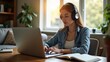 © pondolar - Young woman wearing headphones, working on a laptop in a bright home office
