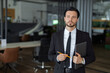 © Andrii Zastrozhnov - A man in a suit holding a pencil and a briefcase. He is standing in a room with chairs and a desk