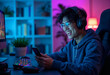 © PhotoPhantom - Happy asia man gamer wear headphone competition play video game online with smartphone colorful neon light in living room at night modern house. Esport streaming game online, Home quarantine activity