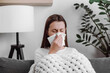 © Yura Yarema - Unhealthy caucasian female blowing nose, coughing or sneezing in tissue. Cold and fever concept. Sick sad young woman sitting on couch covered in warm plaid, suffering from flu, treatment at home