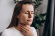 © Yura Yarema - Close up of female suffering from pain sitting on couch at home. Healthcare and medical concept. Unhealthy sad young caucasian woman with sore throat inflamed tonsils from influenza symptoms