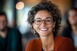 © Odin AI - A woman with curly hair and glasses radiates warmth and friendliness with a broad smile, during an engaging meeting inside a comfortable, modern setting.