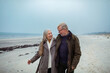 © Marko Geber - Senior couple walking on the beach in winter coats