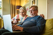 © Marko Geber - Senior couple online shopping on laptop on the couch at home