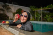 © Odua Images - A cheerful woman enjoys a colorful assortment of fruits while relaxing by the night pool