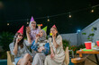 © Odua Images - Friends joyfully celebrating together in festive hats under glowing string lights