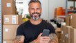 © Pinklife - A confident, tattooed man with gray hair smiles while holding a smartphone in a warehouse surrounded by boxes, representing modern workplace dynamics.