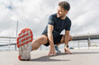 © muse studio - Athlete stretches outdoors on city sidewalk under cloudy sky during daytime workout session