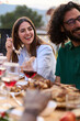 © CarlosBarquero - Vertical. Young adult Caucasian couple smiling sitting at table at friendly summer barbeque outdoors. Joyful millennial people enjoying laughing reunion BBQ food in weekend event eating rooftop