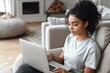© Margarita - Woman Typing on Laptop in Modern Living Room with Curly Hair and Grey T-Shirt