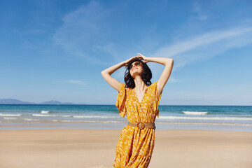 Poster - Woman in yellow dress posing on sandy beach with hands on head in contemplation and relaxation