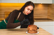 © Maryna - Beautiful female pastry chef adding one cherry to chocolate cake. White kitchen on background.