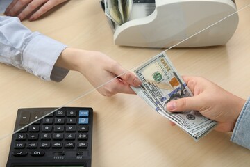 Wall Mural - Client giving dollar banknotes to cashier at table in money exchange, closeup