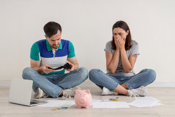 Wall Mural - Young man looking into his empty wallet while his wife crying on floor at home. Bankruptcy concept