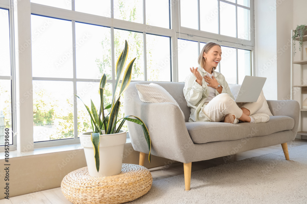 Young woman with laptop video chatting on sofa at home