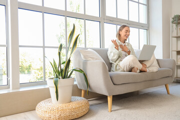 Canvas Print - Young woman with laptop video chatting on sofa at home