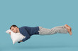 © Pixel-Shot - Young man flying while sleeping on blue background