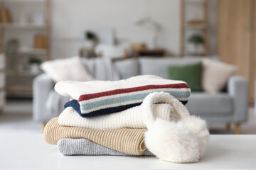 Wall Mural - Stack of folded winter clothes with earmuffs on table in room, closeup