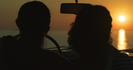 Wall Mural - Couple, sunset and view of beach in car with silhouette, sightseeing or travel adventure with break. Lesbian people, road trip and scenery of ocean on weekend vacation and bonding together in nature