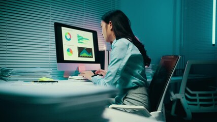 Wall Mural - Businesswoman is working late in her office, illuminated by the glow of her computer screen. She is analyzing charts and graphs, surrounded by paperwork