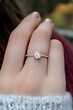 © Sri - A close-up of a hand displaying a diamond engagement ring against a blurred background.