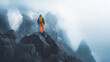 © coramax - Hiker stands on rocky peak surrounded by misty mountains at dawn in a remote wilderness area