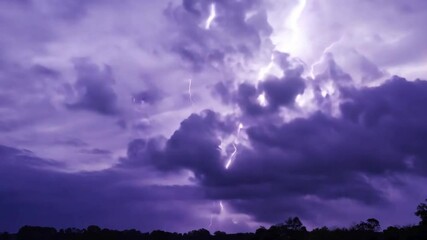 Aufkleber - An intense thunderstorm rolls over the landscape as vibrant purple skies are illuminated by striking bolts of lightning. The atmosphere is charged and dramatic as evening descends.