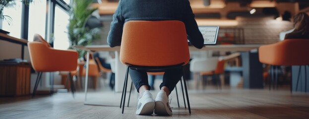 Poster - A person working on a laptop in a modern office setting with orange chairs.