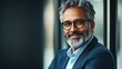 © AbstractAI - Professional headshot of a smiling middle-aged businessman with glasses, showcasing a confident expression against a blurred grey background in an office setting.