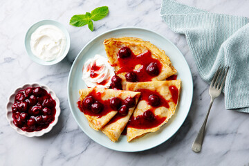 Wall Mural - Crepes, thin pancakes with cherry, berry sauce and whipped cream. Marble table background. Top view.