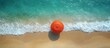 © NeuralNiche - Aerial view of a vibrant orange umbrella on a sandy beach with gentle waves and clear turquoise waters in bright sunlight.