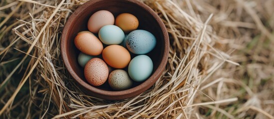 Poster - Colorful Easter eggs nestled in a clay bowl surrounded by natural straw for a vibrant spring celebration atmosphere.