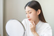© KMPZZZ - Expression worry asian young woman hand touching pustule around the chin and mouth, allergic when wear mask, makeup, show squeezing pimple spot from face. Beauty care, skin problem by acne treatment.