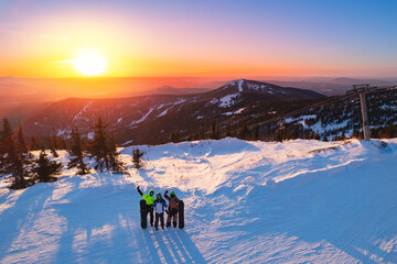 team friends snowboarders, skier stands with ski and snowboard in hands background blue sky with sun
