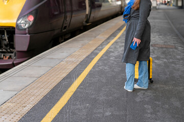 Waiting for a train at a busy station with a suitcase and a blue scarf in cool weather