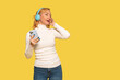 © Iryna - Joyful woman listening to music with headphones while holding a smartphone in front of a bright yellow background
