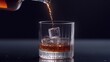 © banzeo - Amber liquid pouring into a rocks glass with ice cubes on a dark background.