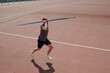 © pressmaster - Athlete running on red track field holding javelin above shoulder and preparing release. Background includes part of stadium and fencing surrounding track field