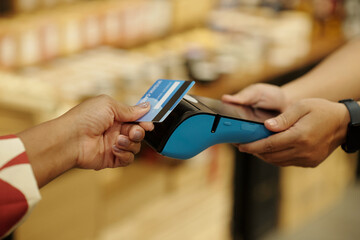 Hand holding credit card while swiping on payment terminal in retail environment. Close-up focus on transaction process and card reader technology