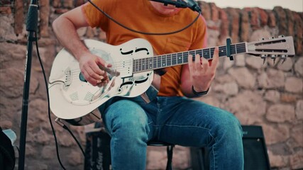 Wall Mural - Close up of a man playing a golden esonator guitar on the street