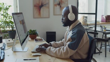 Medium side shot of black male software developer with disability, using wheelchair, sitting at desk at IT startup, typing prompts while testing new artificial intelligence image generation program
